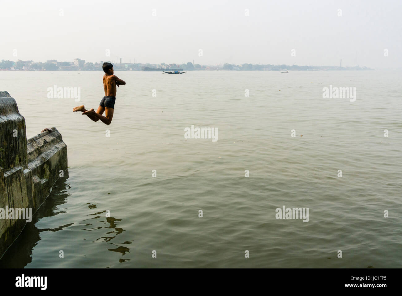 A boy is jumping into the Hoogli River from a wall Stock Photo