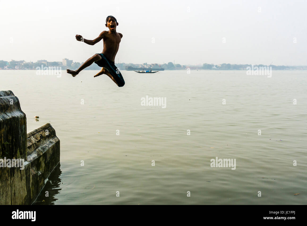 A boy is jumping into the Hoogli River from a wall Stock Photo