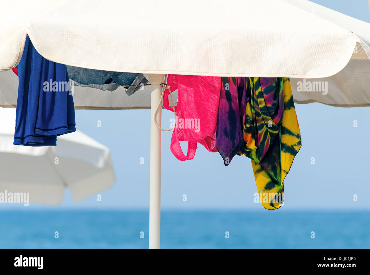 White umbrellas for protection against the sun on a sea beach and the clothes hidden under them. Stock Photo