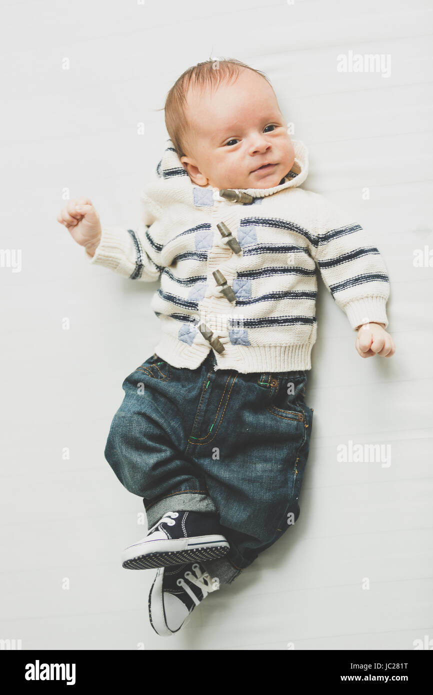 Toned photo of cute baby boy in jeans and sweater lying on bed Stock Photo Alamy