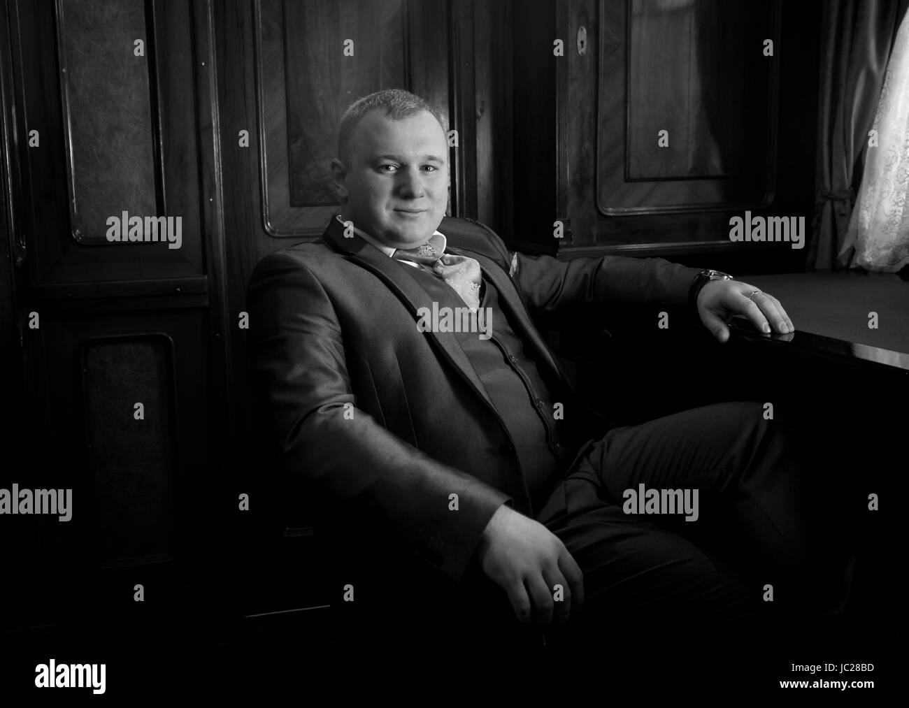 Black and white portrait of stylish man in retro suit sitting in armchair at office Stock Photo