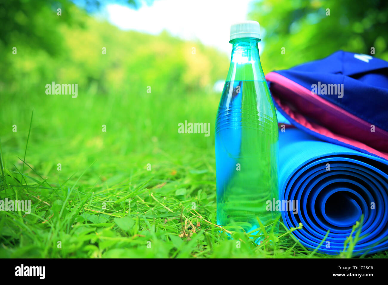 Fitness outdoors background background with copy-space. Water, sport carpet and backpack close-up on green grass. Summer sport background. Stock Photo