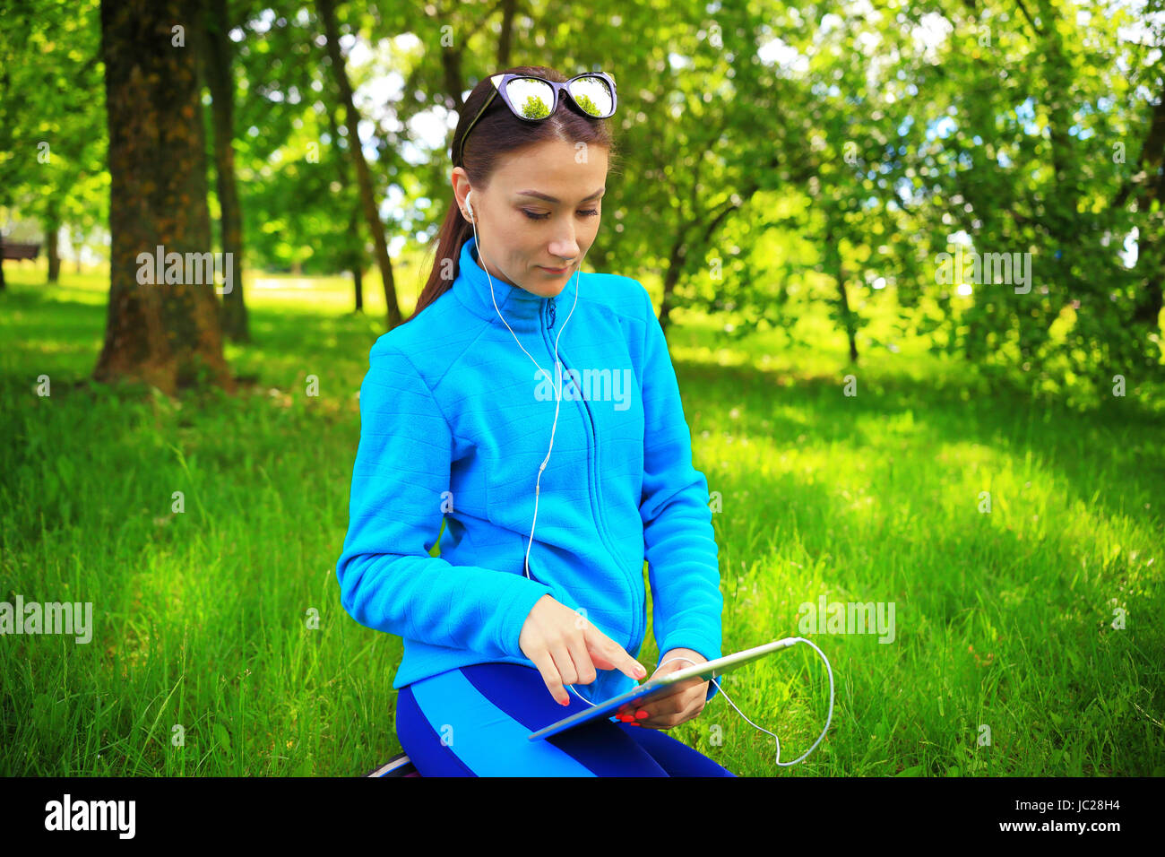 Summer entertainment background. Pretty girl listening music in park. Young brunette woman use tablet. Stock Photo