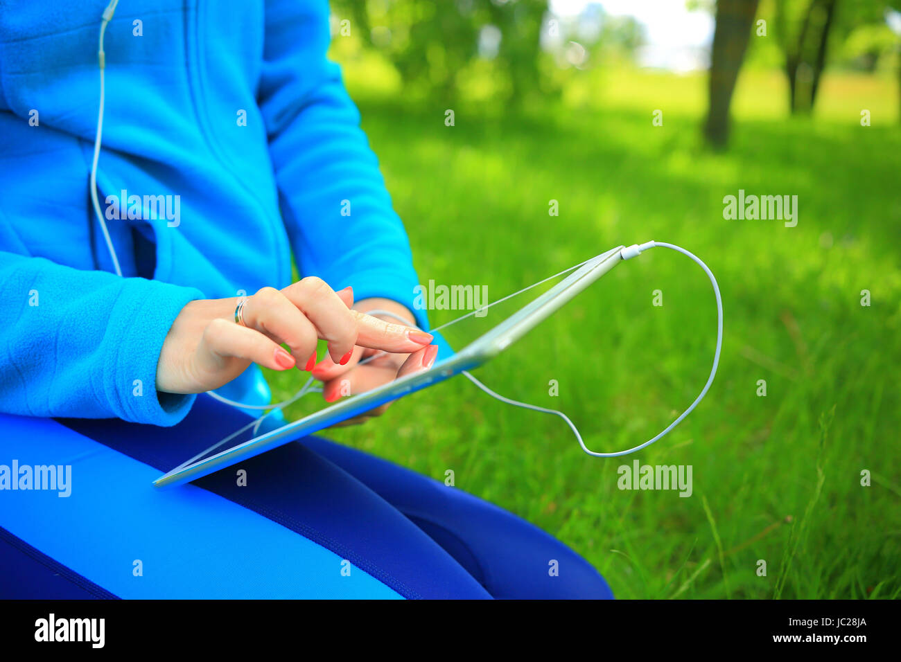 Hands on new tablet close-up. Girl choose music list on tablet in park. Stock Photo