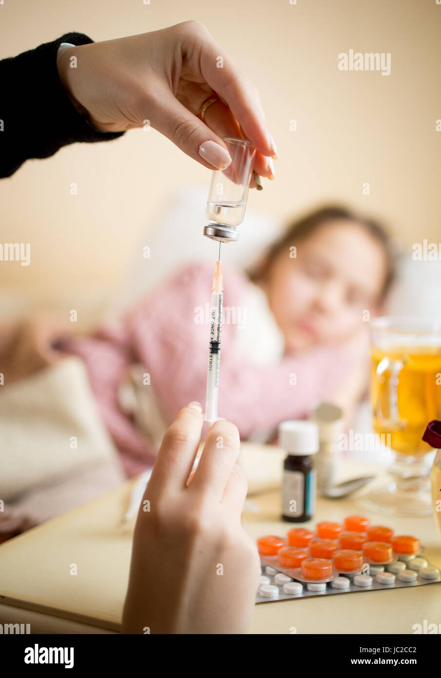 Closeup photo of young woman filling syringe from ampule next to child