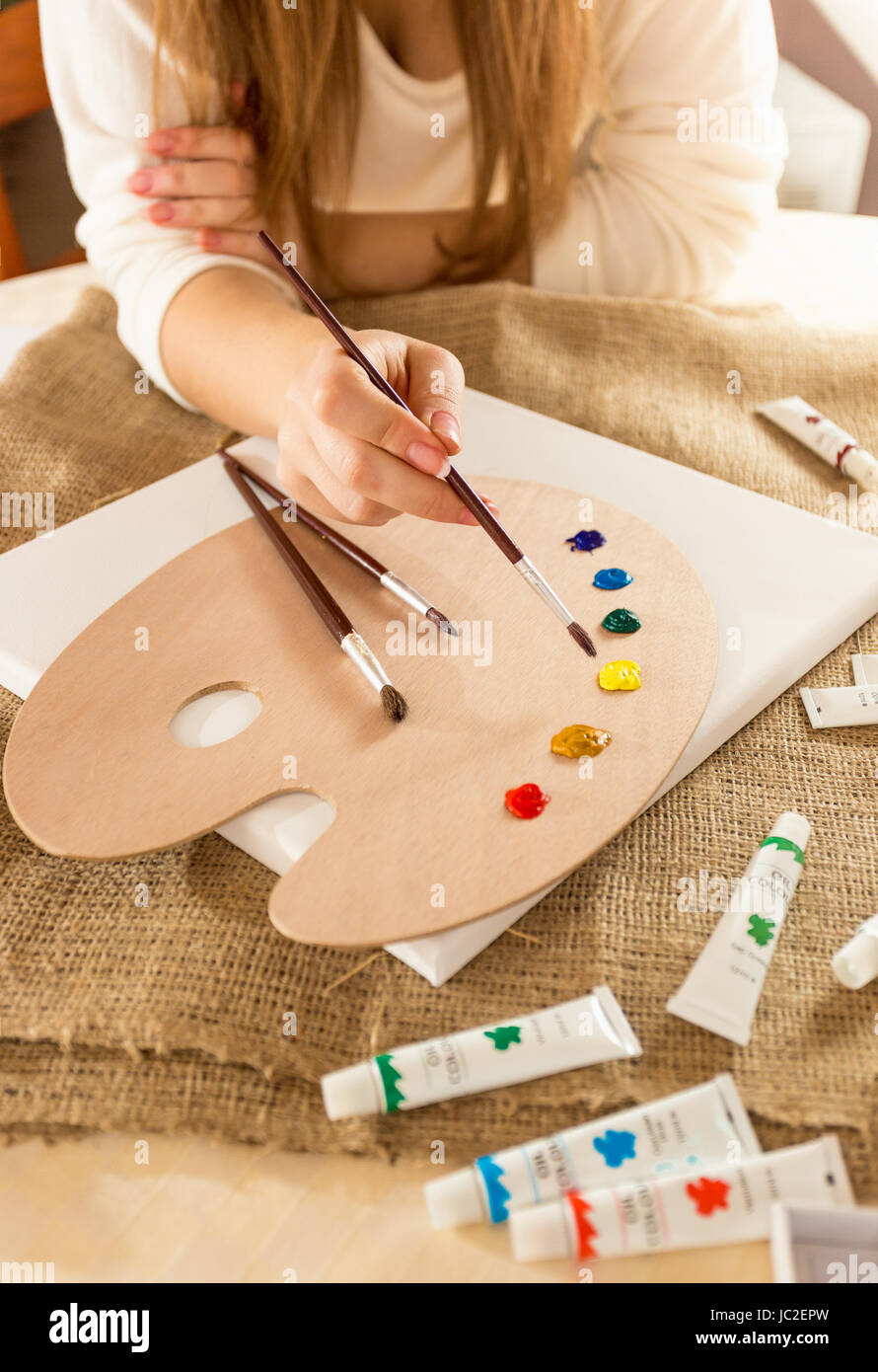 Closeup photo of young female artist sitting at table and drawing on canvas Stock Photo