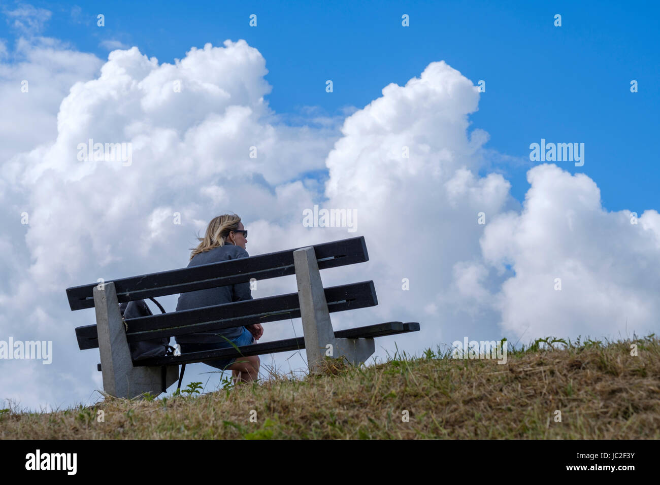 woman sitting on a bench rest and enjoy the view and how the cumulus clouds forming a storm Stock Photo