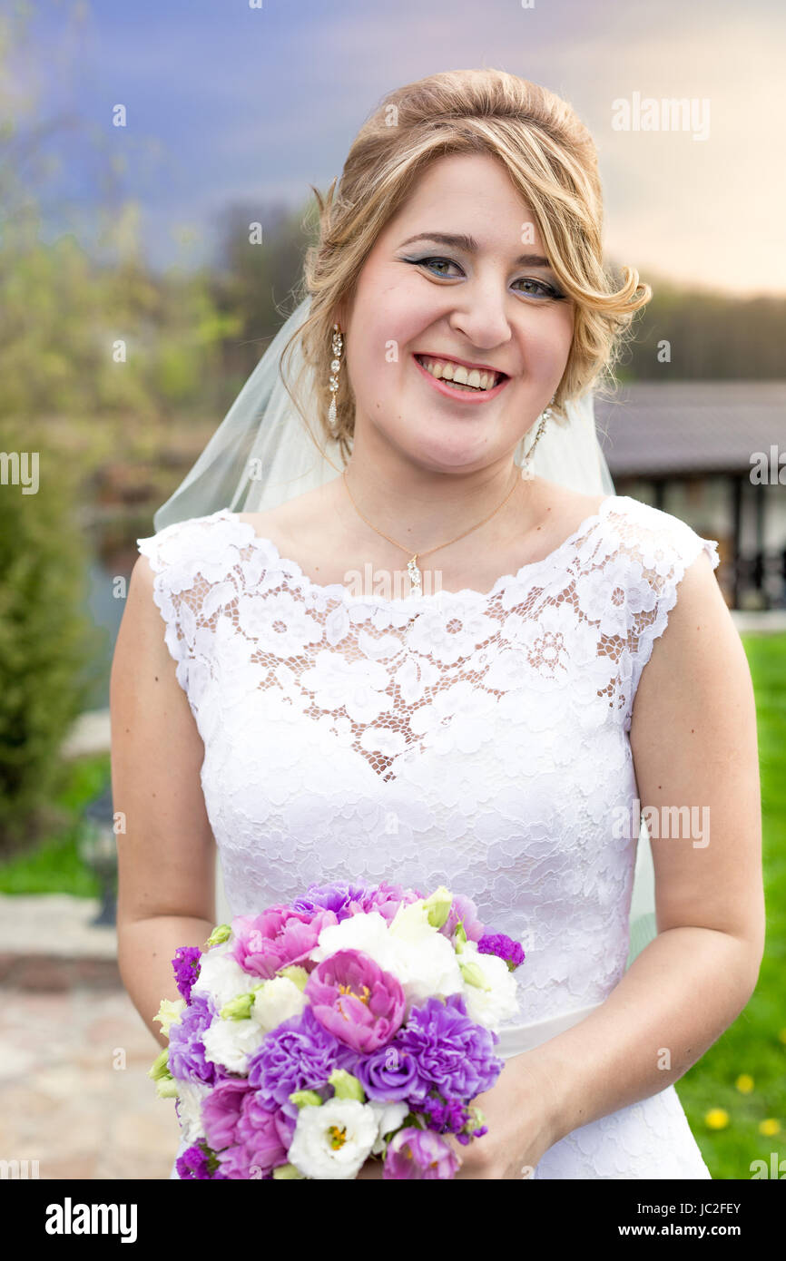 Portrait of laughing blonde bride posing with bridal bouquet outdoors ...