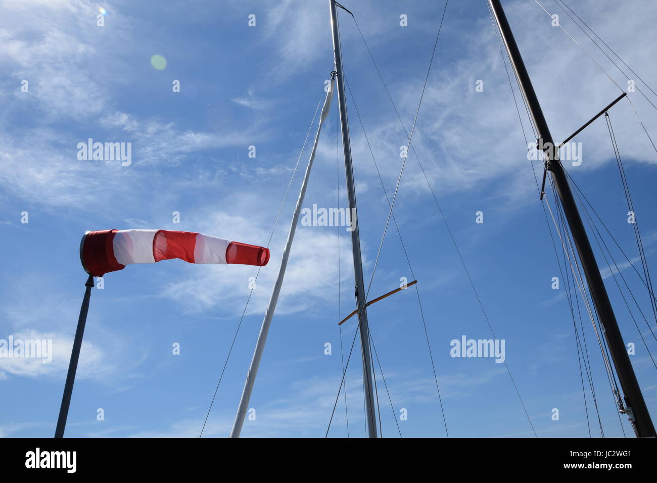 Windsock and yacht masts against blue sky with white clouds Stock Photo