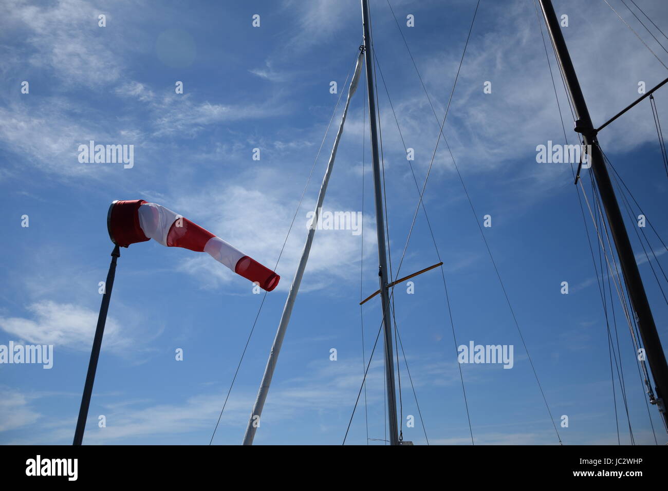 Windsock and yacht masts against blue sky with white clouds Stock Photo