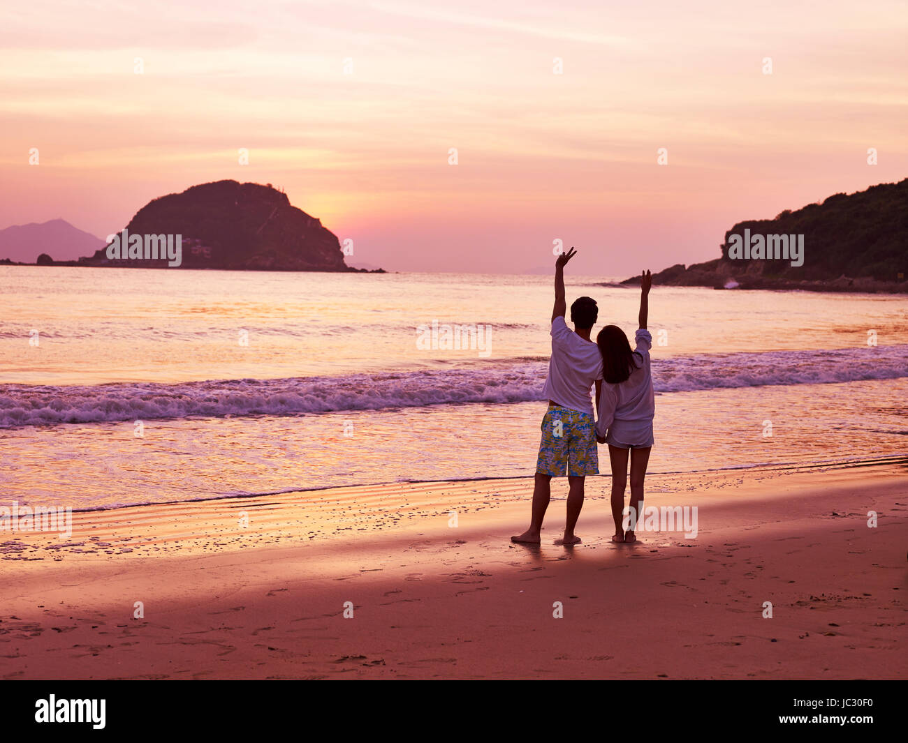 young asian couple taking a walk on beautiful beach before sunrise. Stock Photo