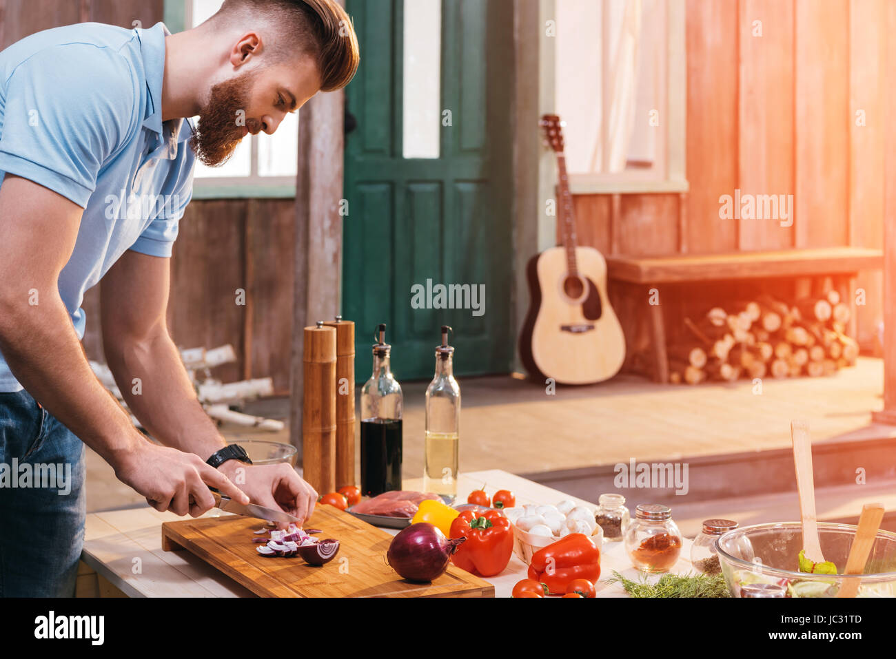 Side view of bearded young man cutting onion for barbecue Stock Photo