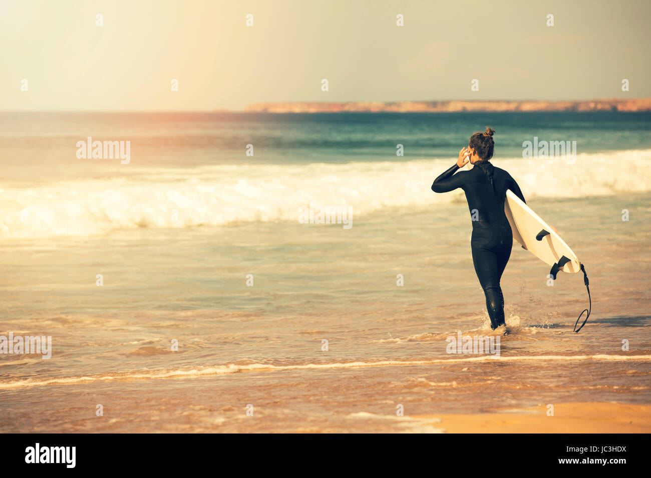 young surfer girl wearing wetsuit going into the ocean to surf at
