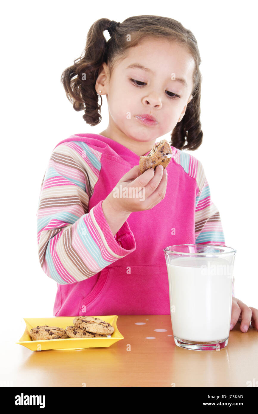Stock image of little girl eating chocolate chip cookies and milk over