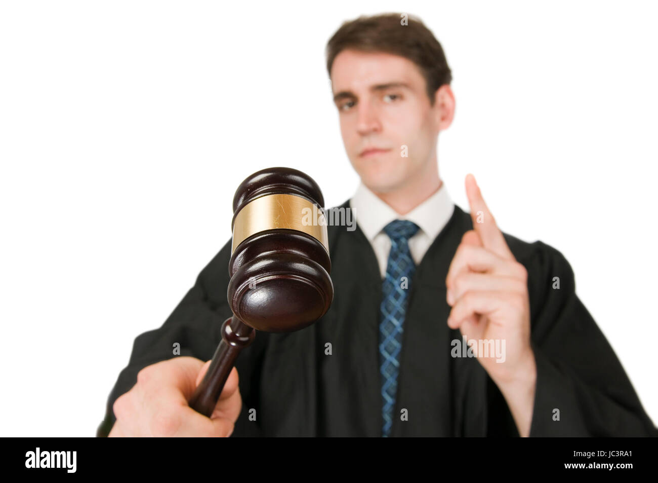 Oberkörperansicht eines jungen Mannes in Richter-Robe vor weissen Hintergrund mit Gravel (Richterhammer) in der rechten Hand ernst und mit erhobenen Zeigefinger in die Kamera blickend Stock Photo