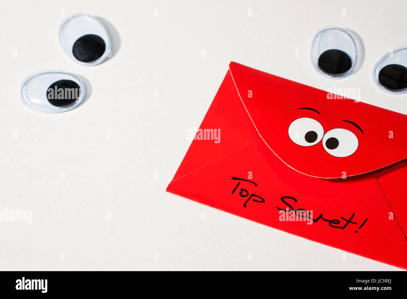 Zwei Paar bewegliche Plastikaugen auf weißem Grund blicken auf einen roten Umschlag mit den Worten 'Top Secret' Stock Photo