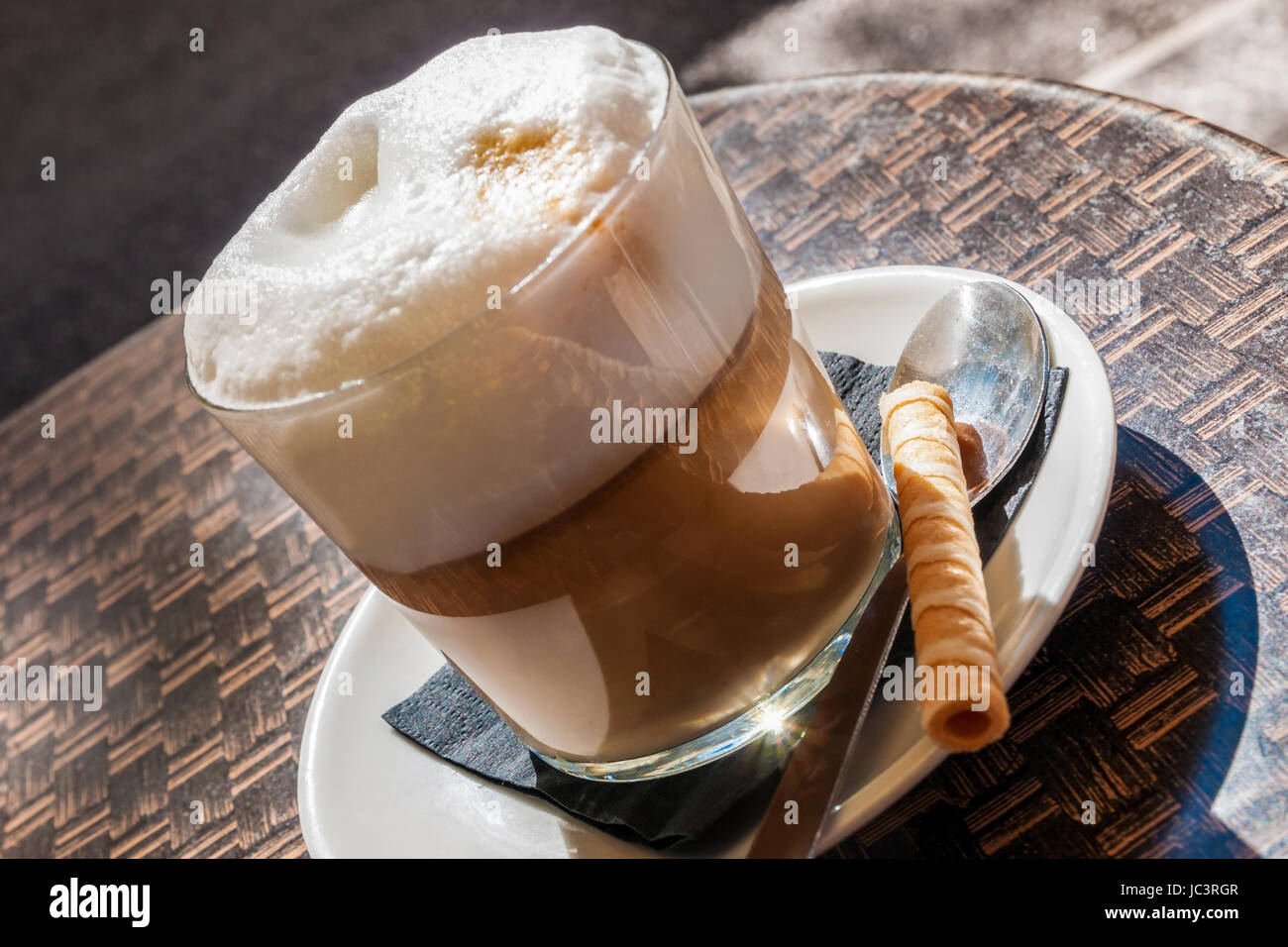 Nahaufnahme eines Glases mit Latte Macchiato und Gebäckröllchen im Sonnenlicht Stock Photo
