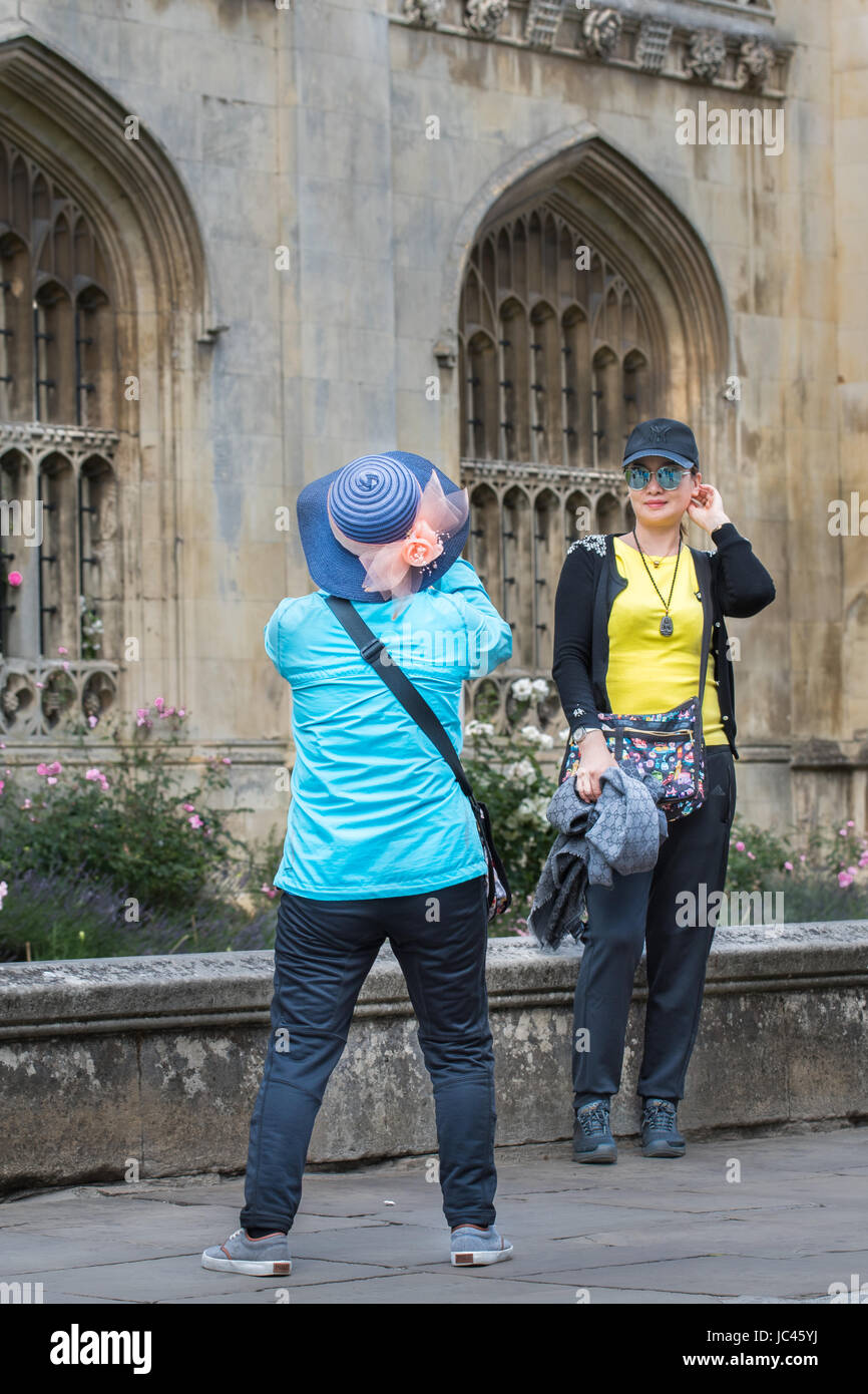 Female chinese tourists, one taking a photograph and the other posing for a photograph, outside the front of King's college, university of Cambridge,  Stock Photo