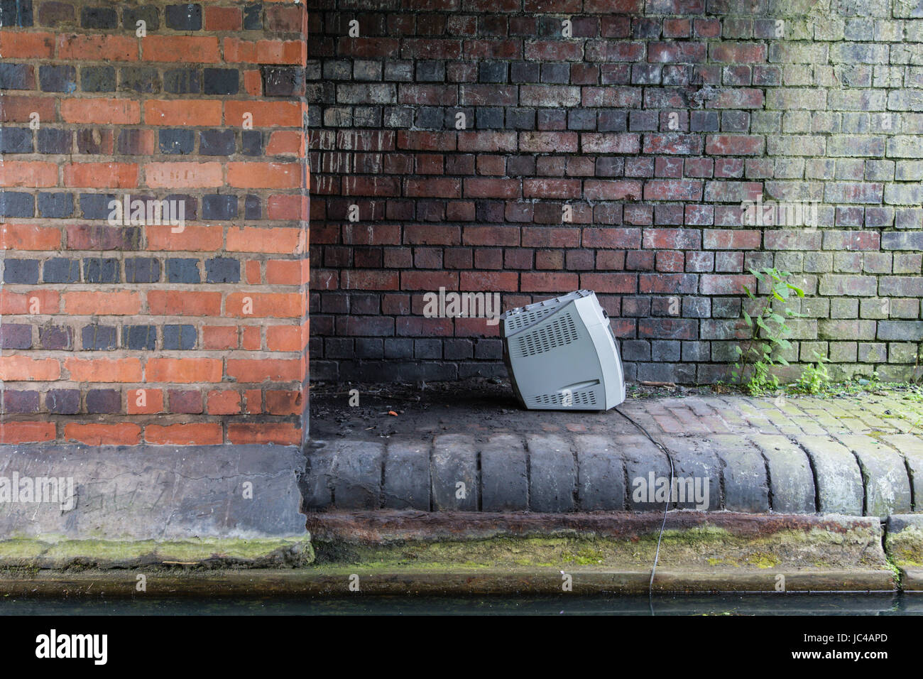 Old TV left by a canal as rubbish garbage UK Stock Photo