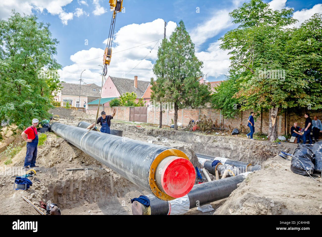 Crane hook with straps is dragging the huge long pipe over dusty ground