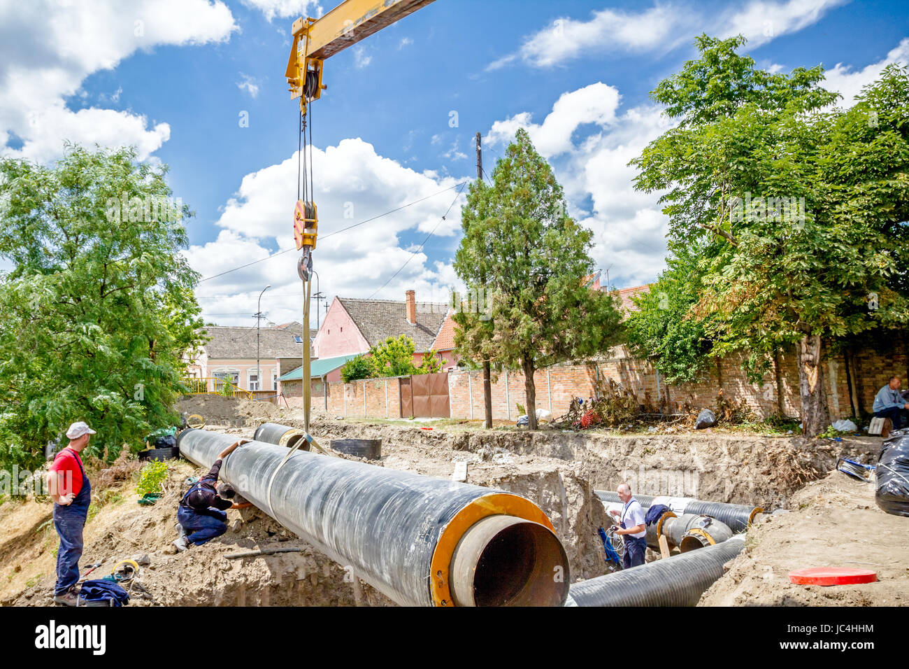 Crane hook with straps is dragging the huge long pipe over dusty ground
