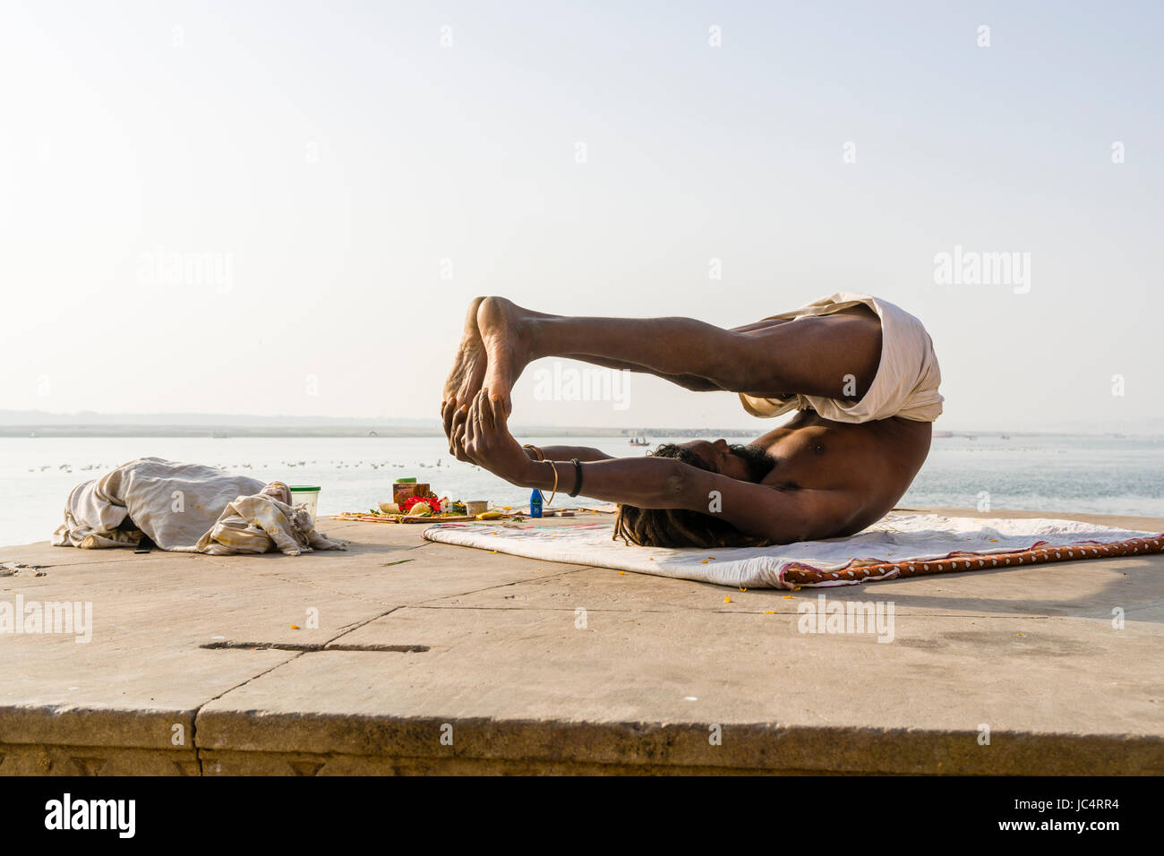 A Sadhu, holy man, is practising yoga asana on a platform at the holy river Ganges at Meer Ghat in the suburb Godowlia Stock Photo