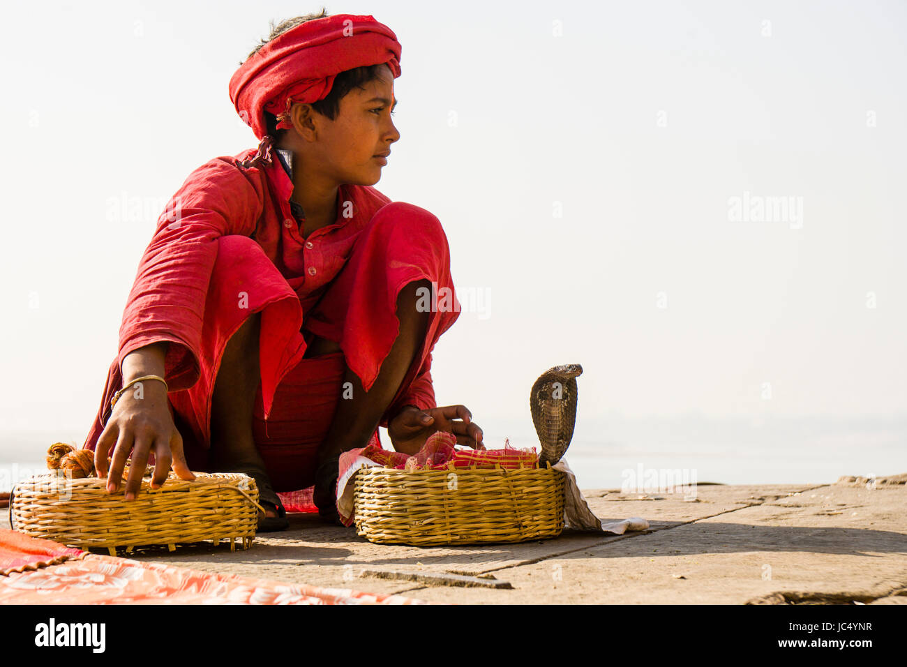 A snake charmer is sitting with his cobras in a basket at the holy river Ganges at Dashashwamedh Ghat, Main Ghat, in the suburb Godowlia Stock Photo