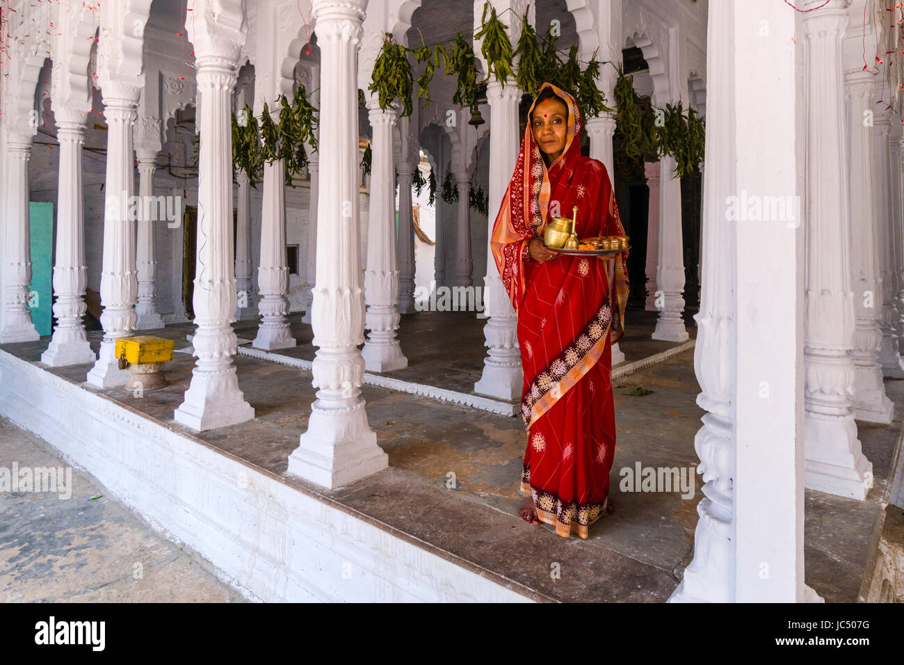 A woman is doing Pooja, offerings to the Gods, in a small hindu temple with white pillars in the suburb Godowlia Stock Photo