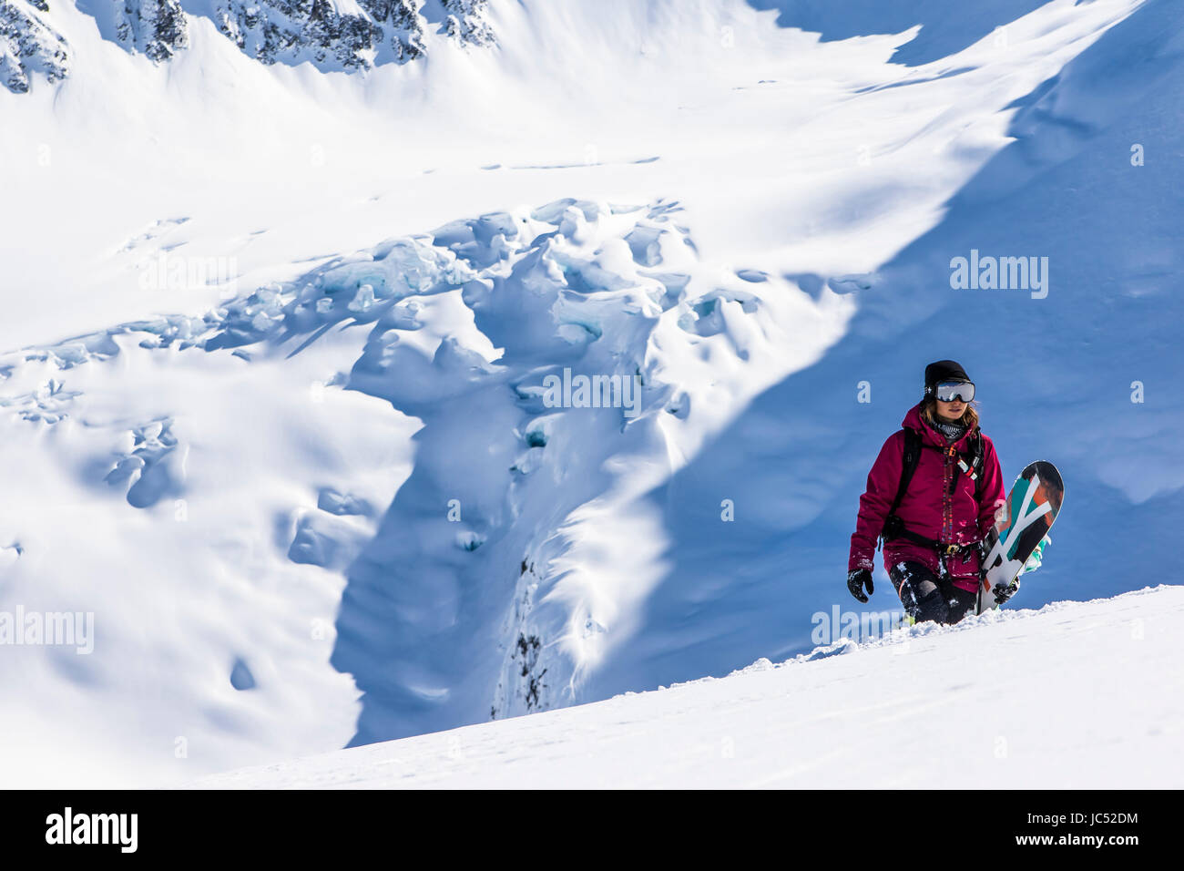 Professional Snowboarder Helen Schettini hikes to a ridge with a glacier in the background on a sunny day in Haines, Alaska. Stock Photo