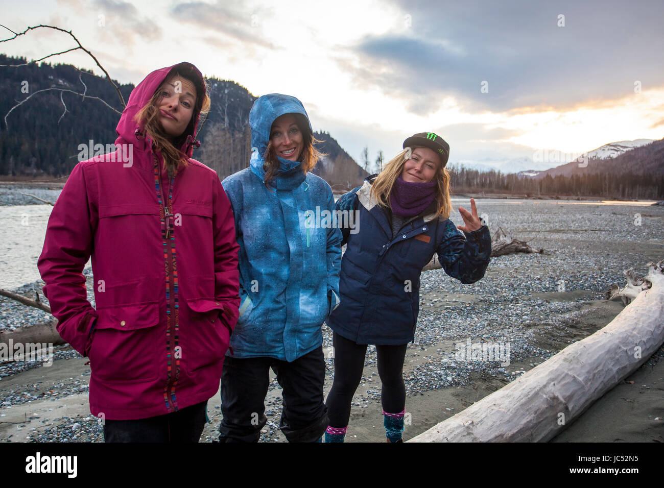 Professional snowboarders Robin Van Gyn, Helen Schettini, and Jamie Anderson, hang out on the side of a river after a day of snowboarding in Haines, Alaska. Stock Photo