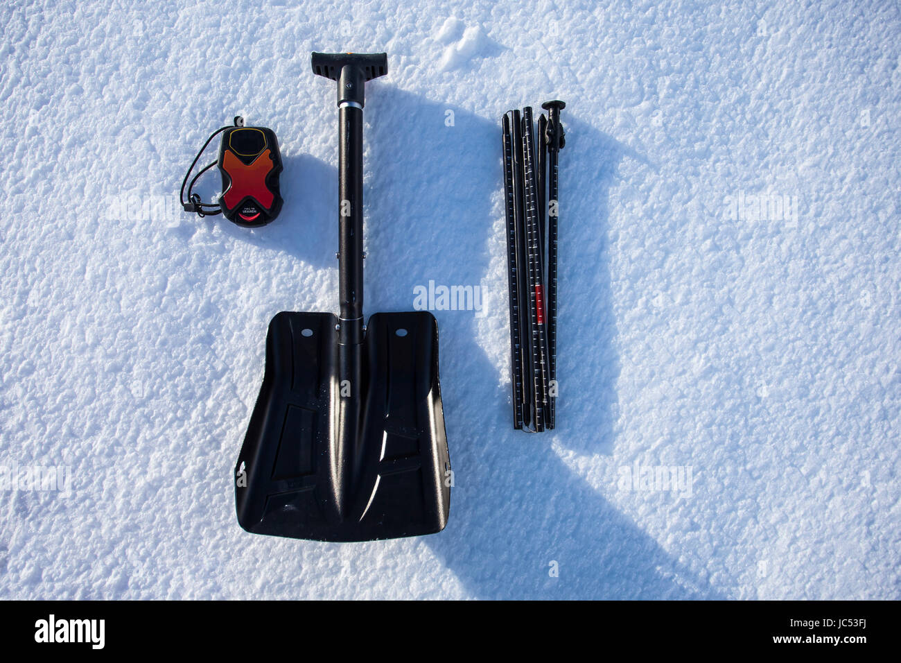 A beacon, shovel and probe, the essentials to a backcountry enthusiasts kit are displayed on the snow. Stock Photo