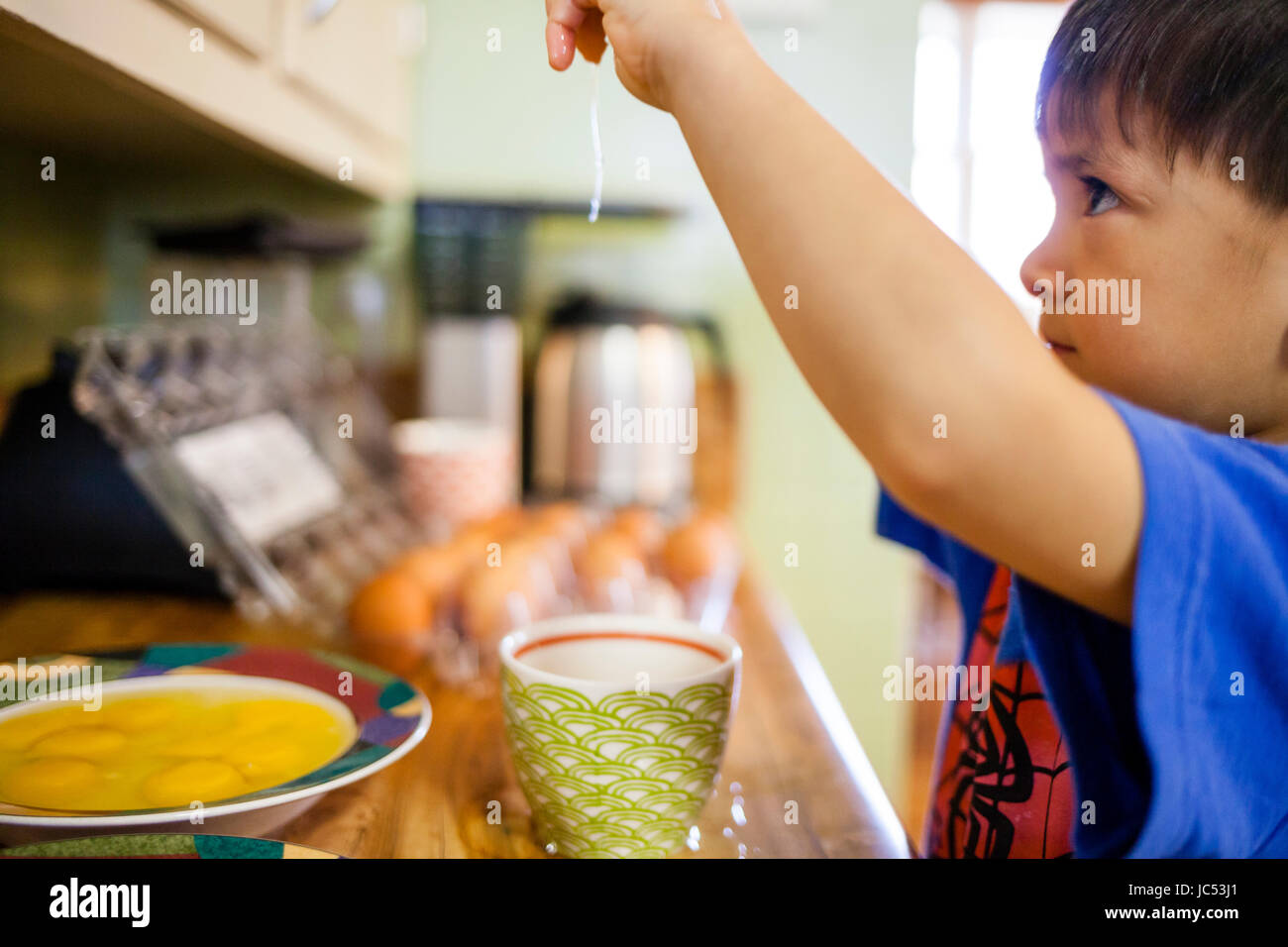 A four year old Japanese American boy helps cook by cracking eggs. Stock Photo