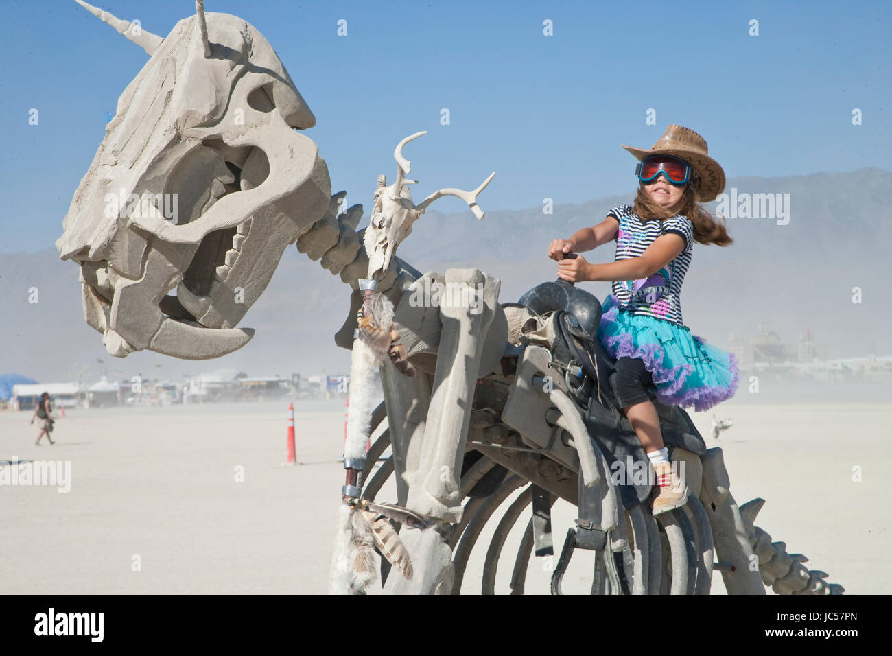 Young girl pretends to ride a dinosaur at Burning Man. This is an example of some of the interactive art at the festival. Stock Photo