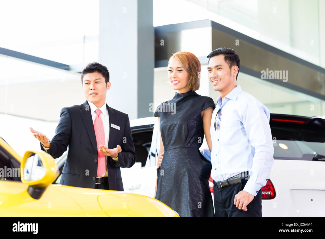 Asian couple buying car in auto dealership consulting the salesman