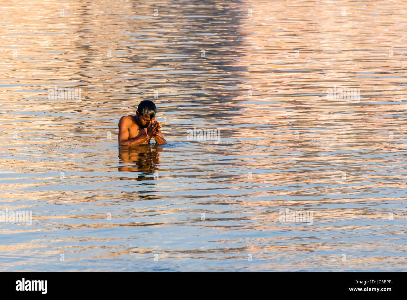 A man, pilgrim, is taking bath and praying on the sand banks at the holy river Ganges Stock Photo