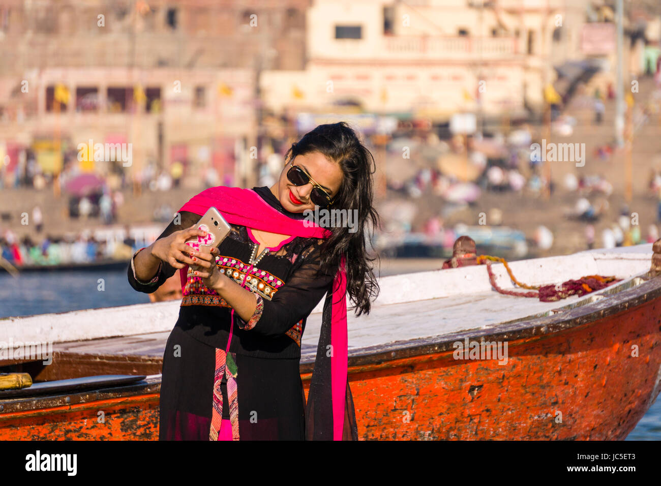 A young modern women are taking selfies on the sand banks at the holy river Ganges, panorama of Dashashwamedh Ghat, Main Ghat, in the distance Stock Photo