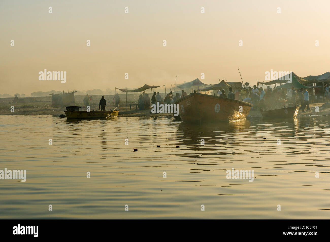 Morning fog is covering boats and pilgrims on the sand banks at the holy river Ganges Stock Photo