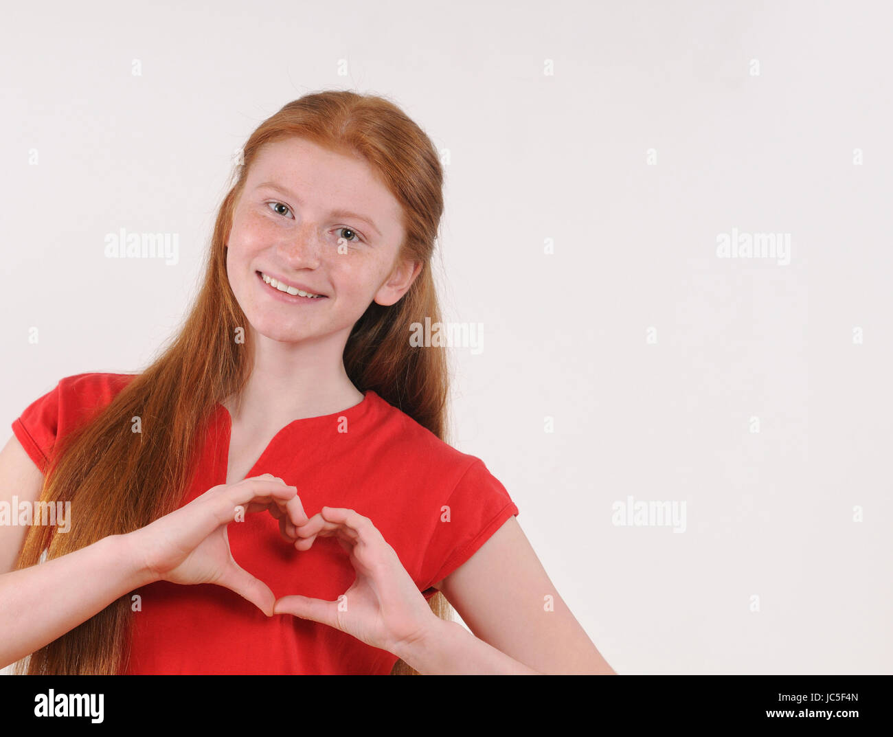 Portrait of a young red hair girl showing heart shape with hands on grey background. Happy smiling lifestyle people concept. Human emotions. Stock Photo