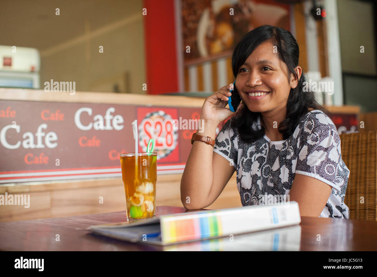 A woman having a drink outside a cafe, talking on her mobile, Indonesia, Asia. Stock Photo