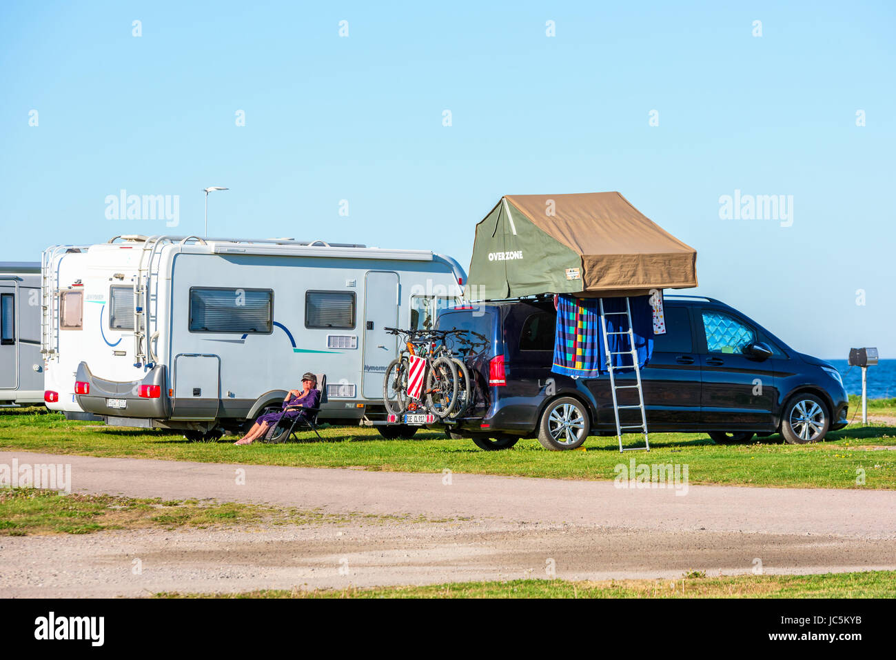 Gronhogen Oland, Sweden - May 28, 2017: Environmental documentary. Foldable tent on top of parked car. Ladder to the ground. Person sitting outside ca Stock Photo