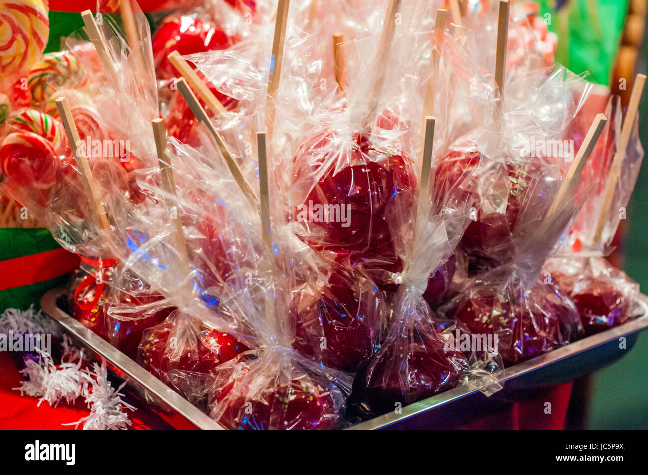 Sweet glazed red toffee candy apples on sticks for sale on farmer market or country fair. Delicious red candy apples covered with colorful sprinkles.  Stock Photo