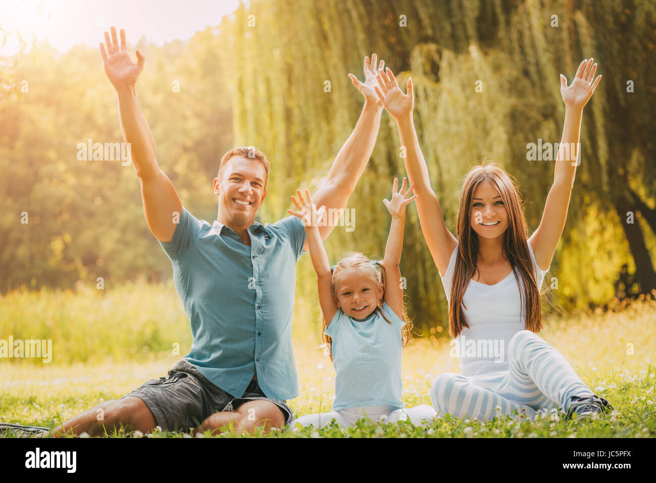Happy smiling family sitting on the grass in the park and having fun ...