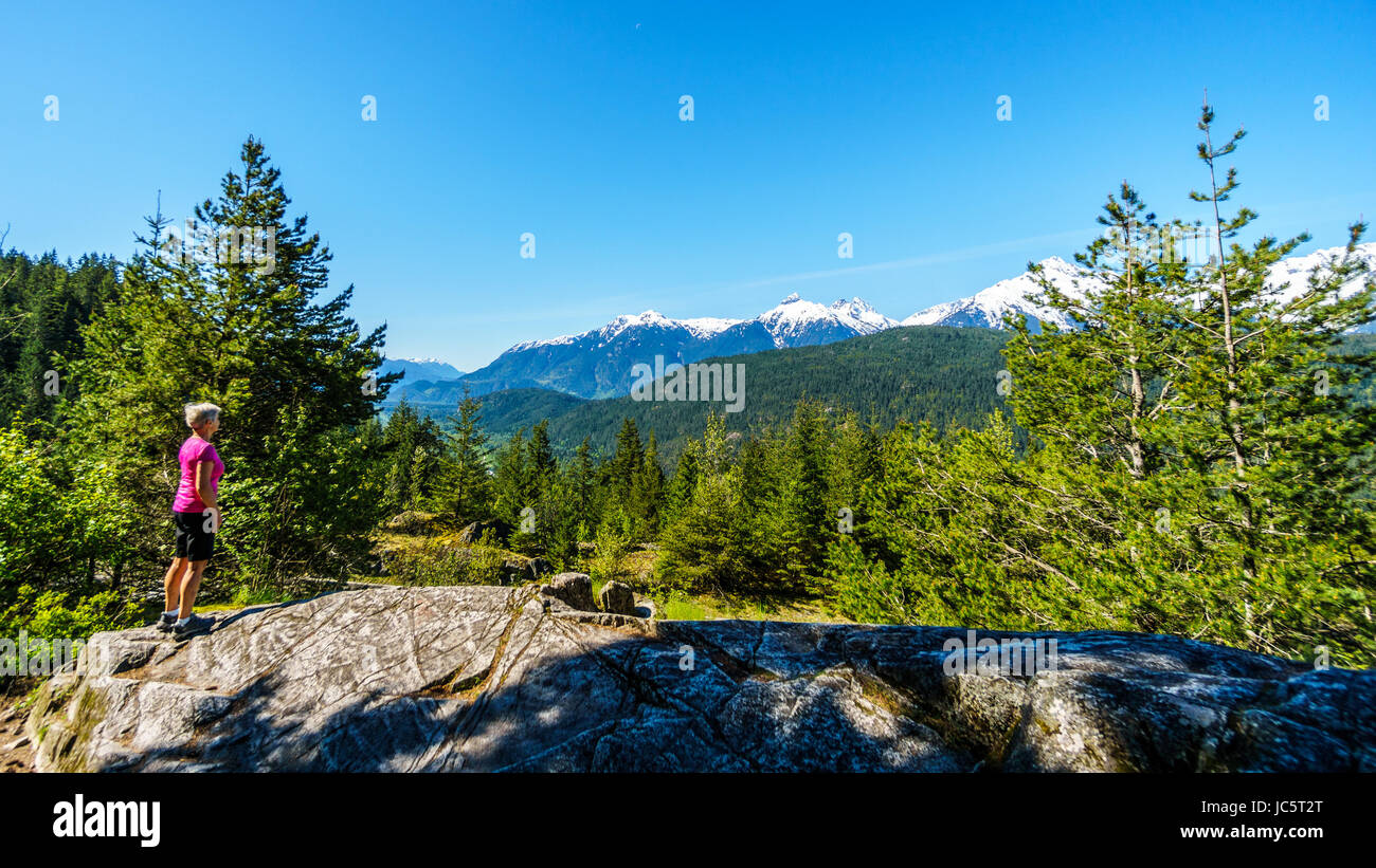 Woman looking at the Tantalus Mountain Range with snow covered peaks of Alpha Mountain, Serratus and Tantalus Mountains along the Duffy Lake Rd Stock Photo