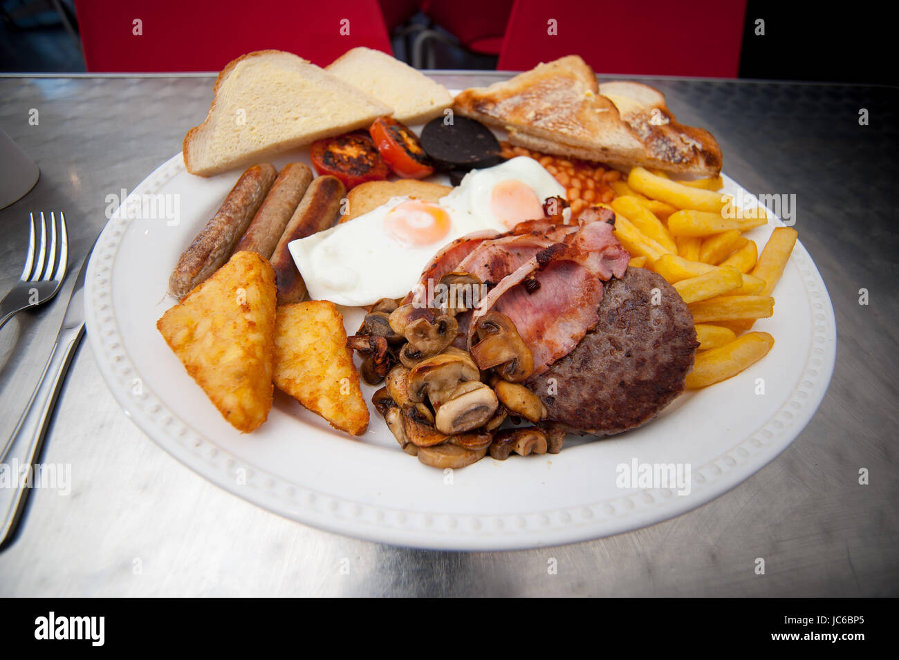 A giant breakfast. Consisting of 2 eggs, 3 bacon, 3 sausage, chips, hash browns, beans, tomatoes, mushrooms, burger, buttered slice, toast. Stock Photo