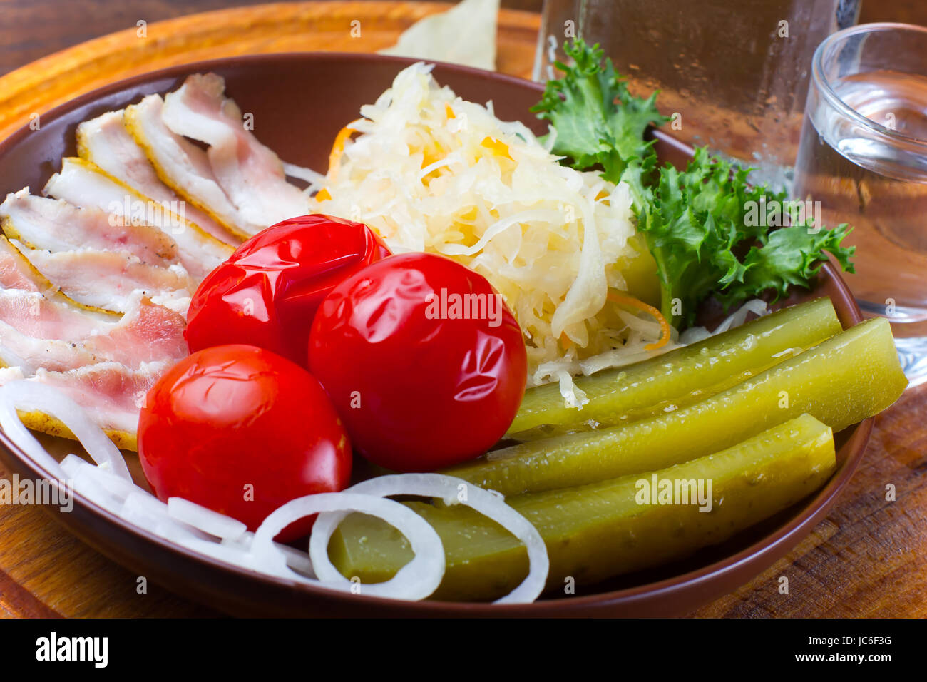 Assorted pickles and pickled vegetables with bacon slices, served on a wooden plate. Stock Photo