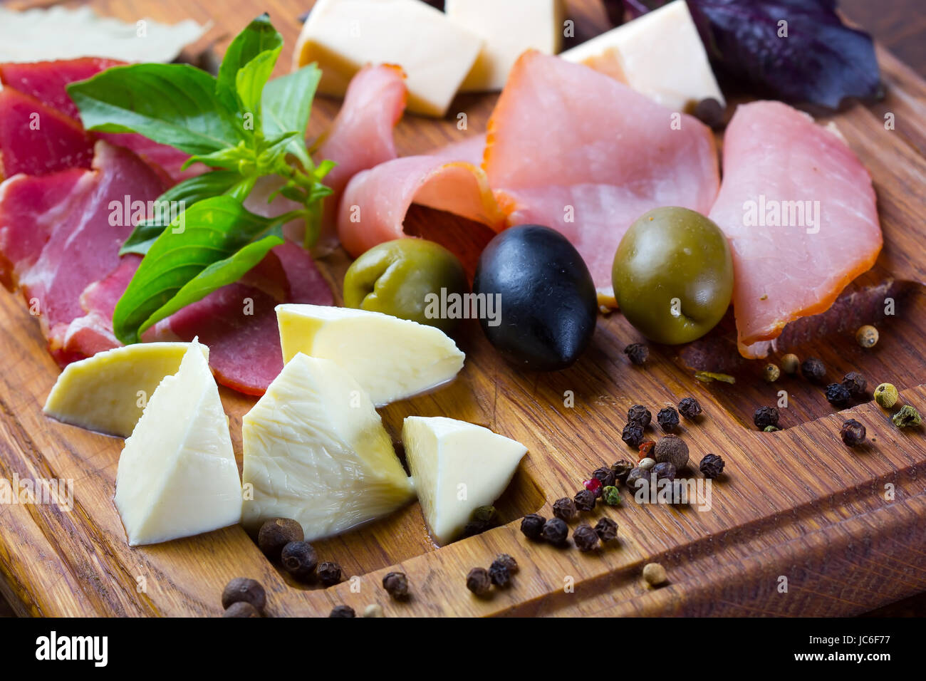 Prosciutto and mozzarella slices with olives ans spices, served on a wooden desk Stock Photo