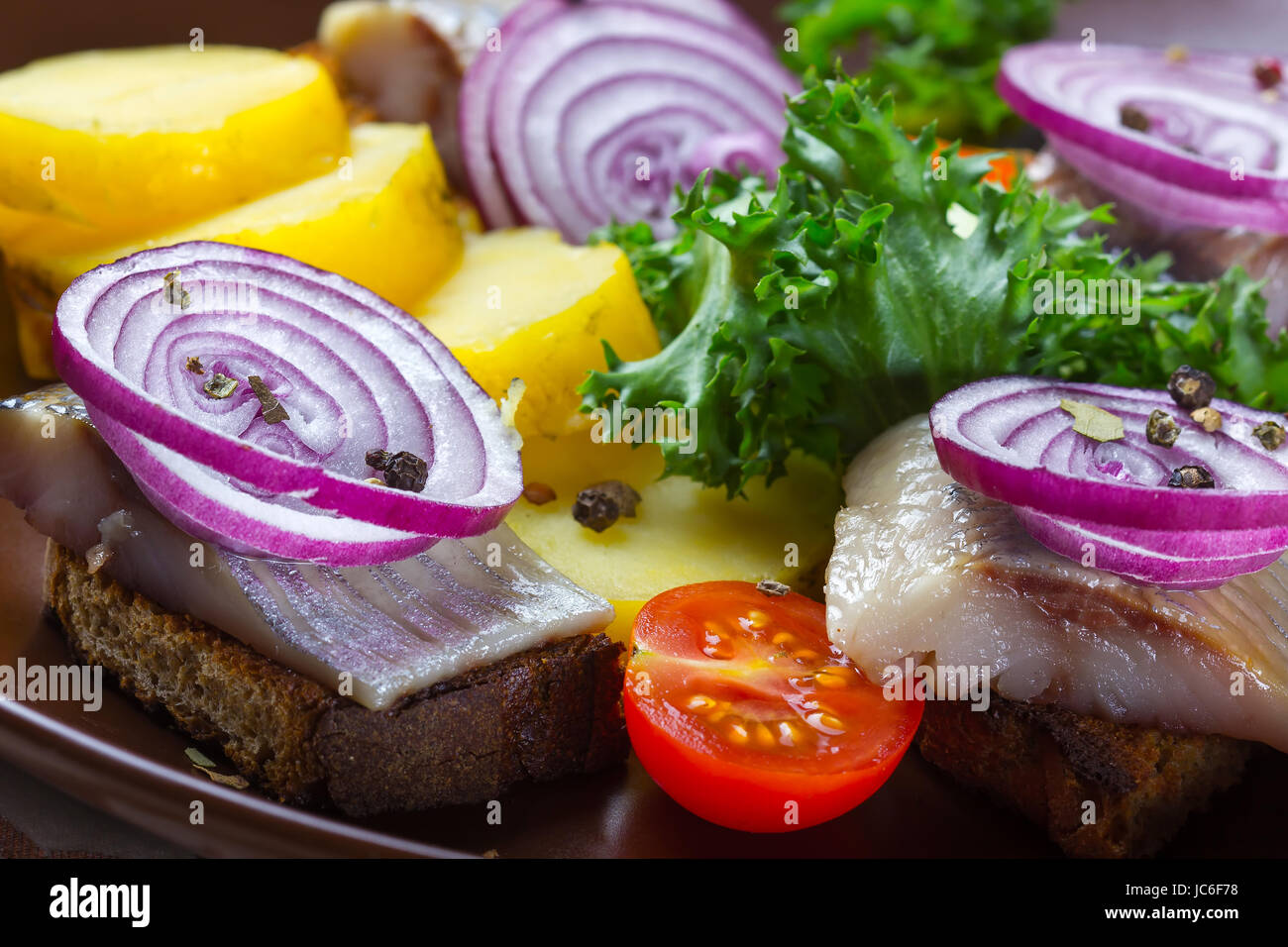 Sandwiches of rye bread with herring, red onions, herbs and potato slices Stock Photo