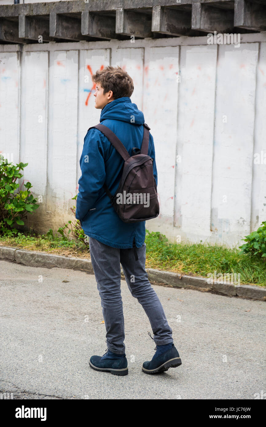 Teenage boy walking alone in city street with backpack, seen from the ...