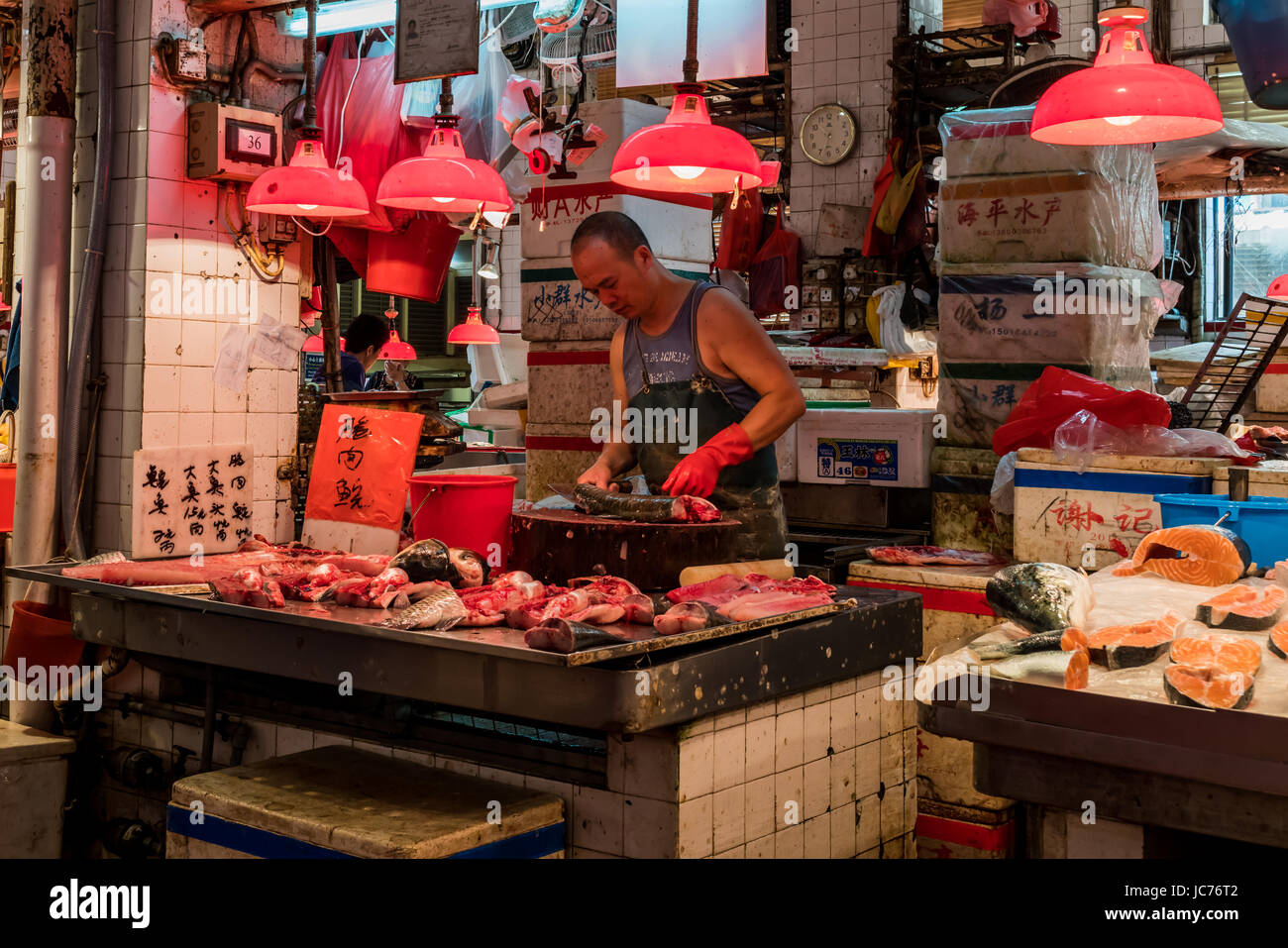 Colourful photo of a fishmonger filleting a fish on a round cutting board in his cramped stall in a wet market in Macau. Stock Photo