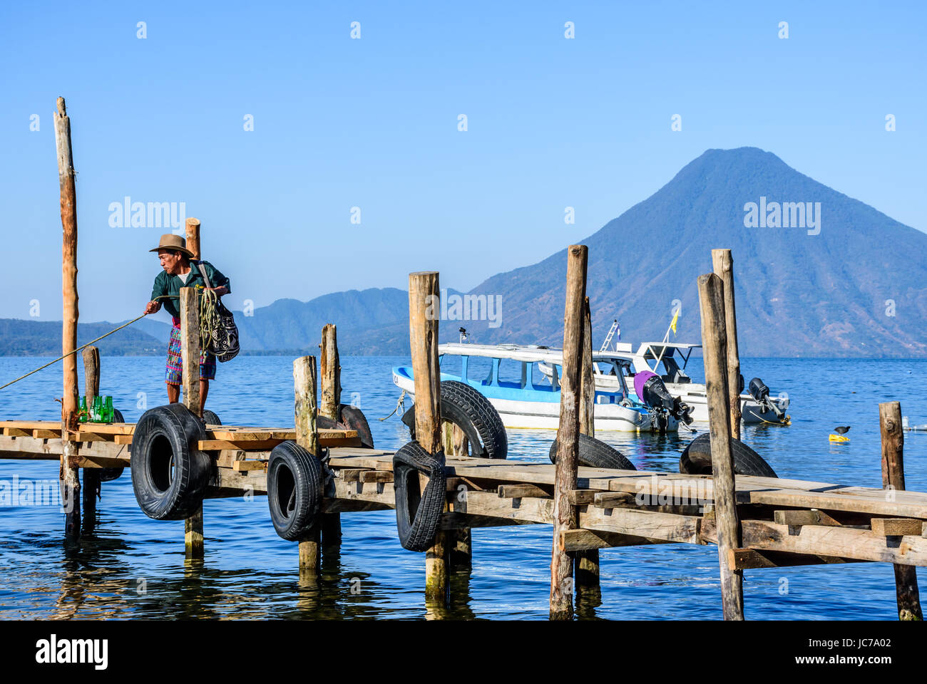 Lake Atitlan, Guatemala - April 4, 2016: Local man dressed in traditional Mayan pants pulls in boat with San Pedro volcano behind. Stock Photo